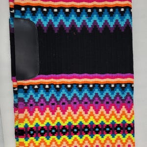 Peut inclure: Tapis de selle de cheval coloré avec un centre noir et des motifs géométriques vibrants en violet, rose, orange, jaune et bleu. Le tapis a un patch en cuir noir sur le côté gauche et une bordure violette.