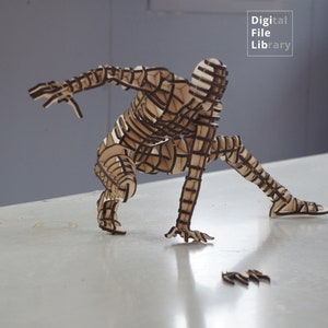 May include: A wooden sculpture of a person in a crouching pose. The sculpture is made of many thin pieces of wood that are layered together to create a 3D effect. The sculpture is painted brown and black.
