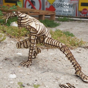 May include: A wooden sculpture of a person in a dynamic pose, with the body constructed of layered, interlocking pieces. The sculpture is made of light brown wood with dark brown accents, and is standing on a gravel surface.