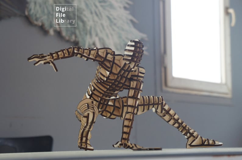 May include: A wooden sculpture of a person in a dynamic pose, with a layered, grid-like design. The sculpture is made of light brown wood and is standing on a white surface.