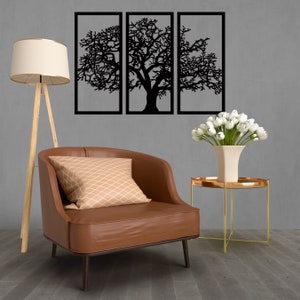 K&ouml;nnte beinhalten: Ein brauner Ledersessel mit einem beigefarbenen, gemusterten Kissen steht vor einer grauen Wand mit drei schwarzen, metallgerahmten Wandbildern, die eine stilisierte Baumsilhouette darstellen.
