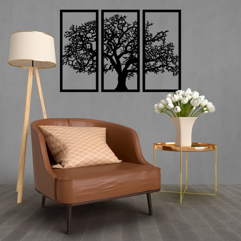 K&ouml;nnte beinhalten: Ein brauner Ledersessel mit einem beigefarbenen, gemusterten Kissen steht vor einer grauen Wand mit drei schwarzen, metallgerahmten Wandbildern, die eine stilisierte Baumsilhouette darstellen.