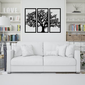 K&ouml;nnte beinhalten: Ein wei&szlig;es Sofa mit zwei wei&szlig;en Kissen steht vor einer wei&szlig;en Wand mit einer schwarzen Metall-Wandkunst in Form eines Baumes. Die Wandkunst ist in drei Abschnitte unterteilt und zeigt einen gro&szlig;en Baum mit &Auml;sten.