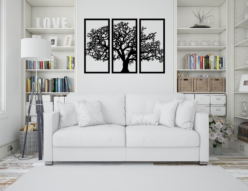 K&ouml;nnte beinhalten: Ein wei&szlig;es Sofa mit zwei wei&szlig;en Kissen steht vor einer wei&szlig;en Wand mit einer schwarzen Metall-Wandkunst in Form eines Baumes. Die Wandkunst ist in drei Abschnitte unterteilt und zeigt einen gro&szlig;en Baum mit &Auml;sten.