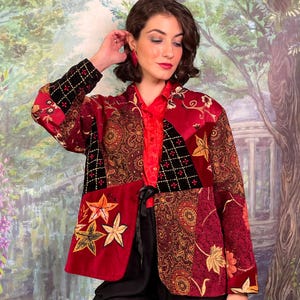 Peut inclure: Veste patchwork aux tons de rouge, bordeaux et noir. La veste présente des motifs floraux et cachemire, avec des appliqués en forme d'étoile. La veste est portée sur un chemisier rouge et un pantalon noir.