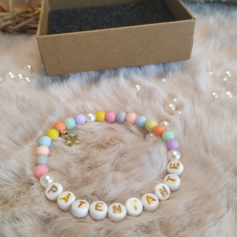 May include: A pastel-colored beaded bracelet with a gold star charm and white beads spelling out the word "PATENTE".