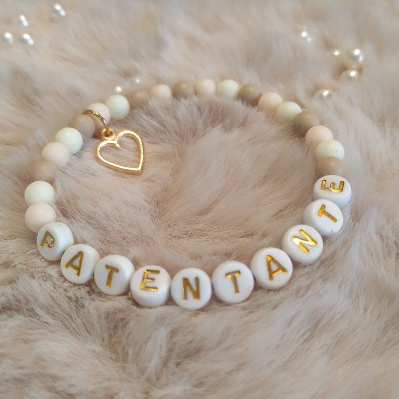 May include: A white beaded bracelet with gold lettering spelling "PATENTANTE" and a gold heart charm.
