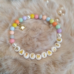 May include: A pastel-colored beaded bracelet with a gold star charm and white beads spelling out the word "PATENTANTE".