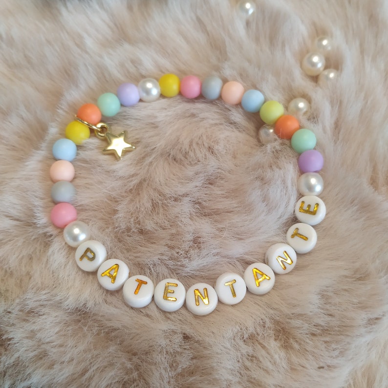 May include: A pastel-colored beaded bracelet with a gold star charm and white beads spelling out the word "PATENTANTE".