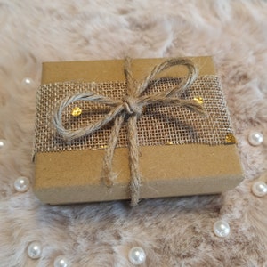 May include: A brown gift box wrapped in burlap ribbon with gold accents. The ribbon is tied in a bow.