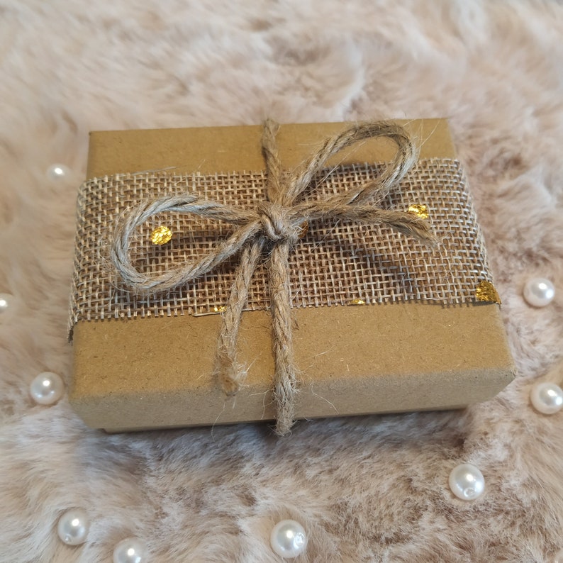 May include: A brown gift box wrapped in burlap ribbon with gold accents. The ribbon is tied in a bow.
