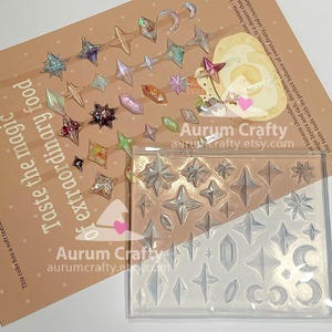 May include: A clear silicone mold featuring various star, diamond, and crescent moon shapes, accompanied by several finished resin charms in matching shapes with iridescent, glittery, and colorful finishes, displayed on a tan paper background.