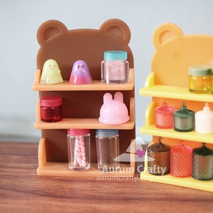 May include: Two miniature wooden shelves with bear ears, one brown and one orange, are filled with miniature jars, bottles, and figurines. The shelves are on a wooden surface.