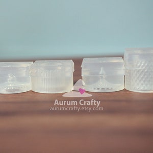 May include: Four clear plastic moulds for making resin crafts. The moulds are square and have different designs.