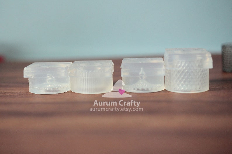 May include: Four clear plastic moulds for making resin crafts. The moulds are square and have different designs.