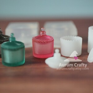 May include: Five decorative glass jars with lids. The jars are in various colours, including black, green, pink, and white. The jars have a vintage style and are perfect for storing small items.