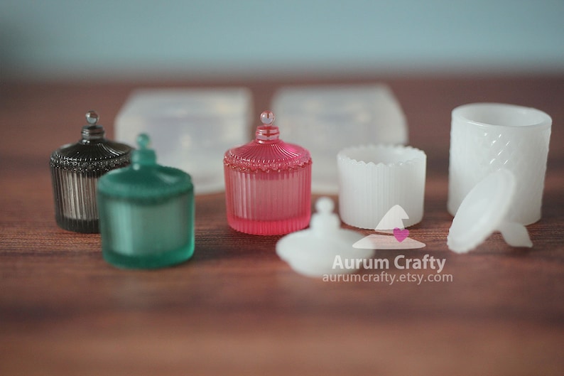 May include: Five decorative glass jars with lids. The jars are in various colours, including black, green, pink, and white. The jars have a vintage style and are perfect for storing small items.