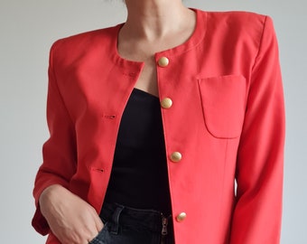 Puede incluir: Una blazer rojo brillante con cuello mandarín y botones dorados. La blazer tiene un bolsillo y se combina con un top negro y una falda vaquera negra.