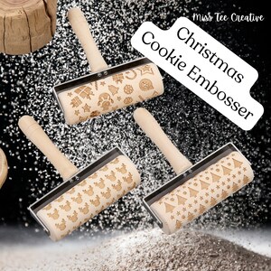 Puede incluir: Tres rodillos de madera con diferentes diseños navideños. Los diseños incluyen renos, árboles de Navidad y copos de nieve. Los rodillos están sobre un fondo negro con polvo blanco.