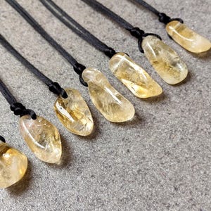 Puede incluir: Ocho colgantes de cristal de citrino amarillo en cordones negros. Los colgantes son de diferentes formas y tamaños, y todos están pulidos hasta obtener un acabado liso.
