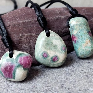 May include: Three green and pink gemstone pendants on black cords. The pendants are all different shapes and sizes. The gemstones are a mix of green and pink.