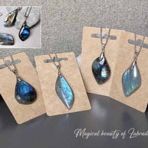 Puede incluir: Cuatro collares de plata con colgantes de piedra de labradorita. Los colgantes son de diferentes formas y tamaños, pero todos tienen un color azul y verde iridiscente similar. Los collares se muestran en cartulina marrón con el texto "Magical beauty of Labradorite".