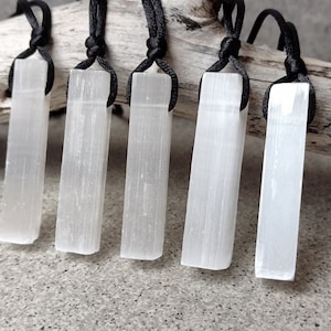 Può includere: Sei ciondoli in cristallo di selenite bianca su cordini neri. I cristalli sono lisci e hanno una texture striata. I cordini sono annodati in cima.