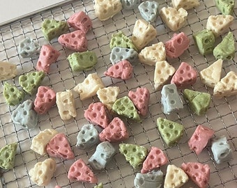 May include: A variety of pastel-colored cheese snacks arranged on a wire rack. The snacks are in the shapes of stars, hearts, and other geometric shapes.