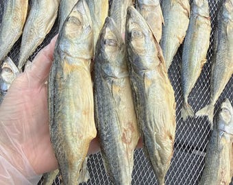 Pode incluir: Uma coleção de peixes secos, dispostos numa bandeja de malha metálica. Os peixes têm um tom cinza prateado com um toque amarelado, e são exibidos em close-up. Os peixes estão inteiros, com barbatanas e caudas visíveis, sugerindo um produto do mar.