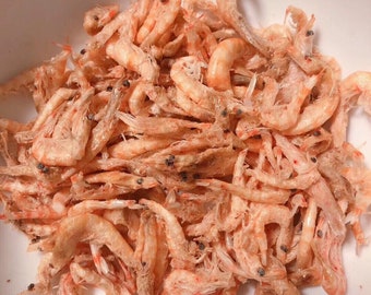 May include: A white bowl filled with dried shrimp. The shrimp are a pale orange color and have a slightly translucent appearance.