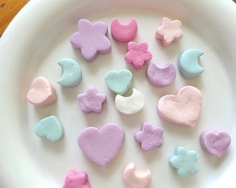 May include: A white plate with a variety of pastel-colored clay shapes, including hearts, stars, and crescent moons.