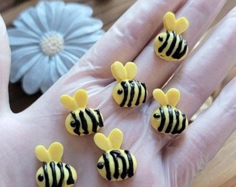 May include: Six small yellow and black bee-shaped decorations. The bees have black stripes and are made of a smooth, glossy material.