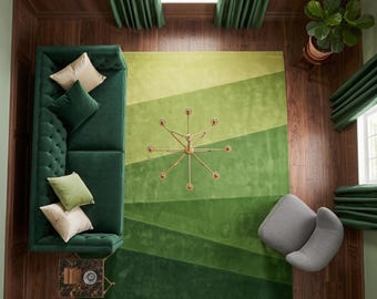 Op de afbeelding: Een rechthoekig vloerkleed met een verloop van groentinten in diagonale strepen, variërend van licht limoengroen tot diep bosgroen. Het kleed ligt op een donkere houten vloer en wordt gedeeltelijk bedekt door een donkergroene gecapitonneerde bank.