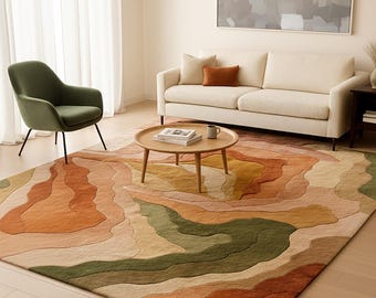 May include: A living room scene featuring a large area rug with a layered, abstract design in shades of orange, green, and beige. A round wooden coffee table sits in the center, with a cream-colored sofa and a green armchair. A large abstract painting hangs on the wall.