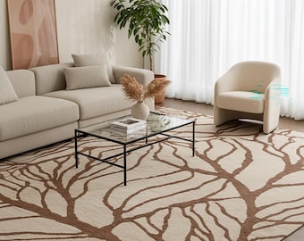 May include: A living room scene featuring a beige sofa, armchair, and a glass-top coffee table with a black metal frame. A large area rug with a brown tree branch design covers the floor. A framed artwork and a potted plant add to the decor.