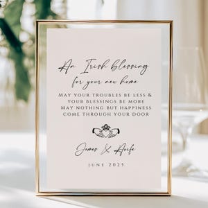 May include: A framed print with a gold border, featuring the text "An Irish Blessing for your new home." The text is in black script, with a Claddagh symbol and the names "James & Aoife" and the date "JUNE 2025" below.