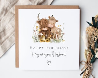 May include: A square greeting card with a watercolor illustration of two Highland cows amidst wildflowers. The card reads "HAPPY BIRTHDAY To my amazing Husband" with a heart symbol. The card is set against a neutral background.