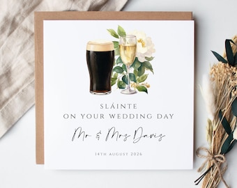 May include: A square wedding greeting card featuring a watercolor illustration of a dark stout beer and a glass of white wine with white flowers and green leaves. Text reads: SLÁINTE ON YOUR WEDDING DAY, Mr & Mrs Davis, 14TH AUGUST 2026.