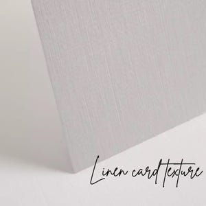 K&ouml;nnte beinhalten: Nahaufnahme einer hellgrauen Karte mit Leinenstruktur. Die Karte ist abgewinkelt und zeigt ihre Kante und die Textur des Papiers. Die Worte "Linen card texture" sind in Schreibschrift geschrieben.