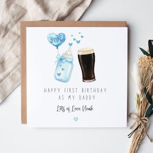 May include: A square greeting card featuring a watercolor illustration of a light blue baby bottle with a blue bow, a blue heart-shaped balloon labeled 2026, and a glass of dark stout beer. Text reads: HAPPY FIRST BIRTHDAY AS MY DADDY, Lots of Love Noah.