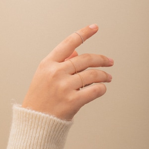 K&ouml;nnte beinhalten: Eine Hand tr&auml;gt drei zarte Ringe aus Gold und Silber. Die Ringe sind d&uuml;nn und haben ein perlenf&ouml;rmiges Design.