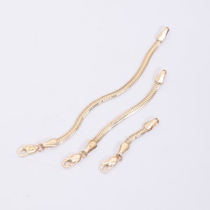 May include: Three gold snake chain bracelets with lobster claw clasps. The chains are different lengths.