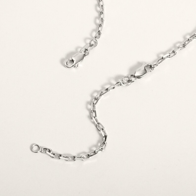 May include: A silver chain necklace with two lobster claw clasps. The chain is made of small, oval-shaped links.