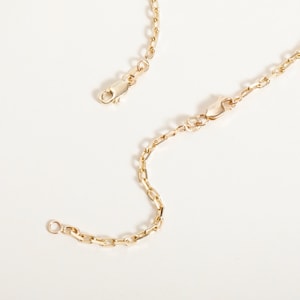 May include: A gold chain necklace with a lobster clasp closure. The chain is made of small, linked oval shapes.