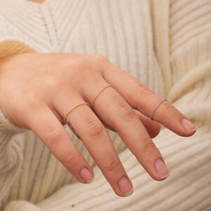 K&ouml;nnte beinhalten: Nahaufnahme einer Hand, die drei zarte goldene und silberne Perlenringe tr&auml;gt. Die Ringe sind d&uuml;nn und schlicht, mit kleinen Perlen, die einen dezenten Glanz erzeugen.