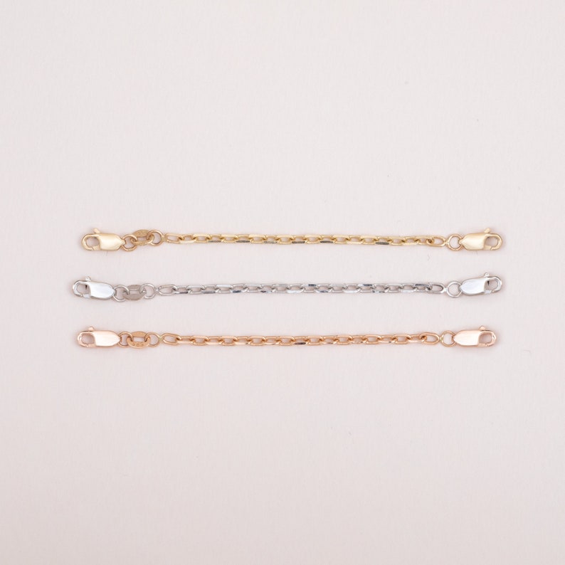May include: Three gold chain extenders, one in yellow gold, one in white gold, and one in rose gold. Each extender has a lobster clasp on each end.