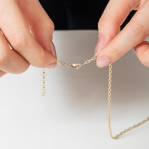 May include: A gold chain necklace with a lobster clasp closure. The chain is made of small, linked ovals.