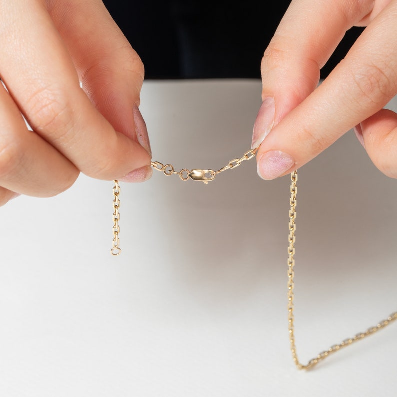 May include: A gold chain necklace with a lobster clasp closure. The chain is made of small, linked ovals.