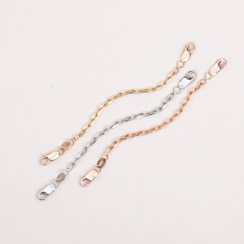 Three gold chain extenders, one in yellow gold, one in white gold, and one in rose gold. Each extender has a lobster clasp.