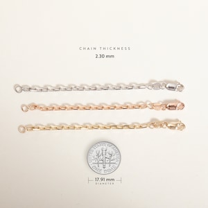 May include: Three chain links of different metals, silver, rose gold, and gold, are laid out horizontally on a white background. A US dime is placed below the chains for size comparison. The text "CHAIN THICKNESS 2.30 mm" is above the chains. The dime has the text "UNITED STATES OF AMERICA ONE DIME" and "17.91 mm DIAMETER" printed on it.